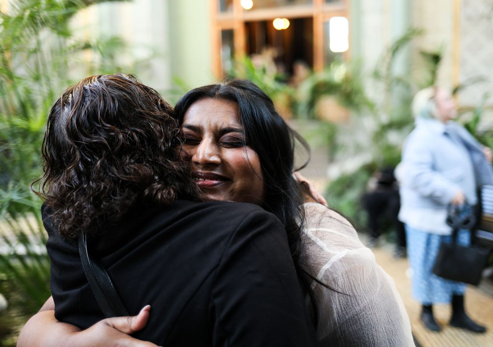 Duas mulheres num abraço emocionado, uma delas de olhos fechados e sorrindo