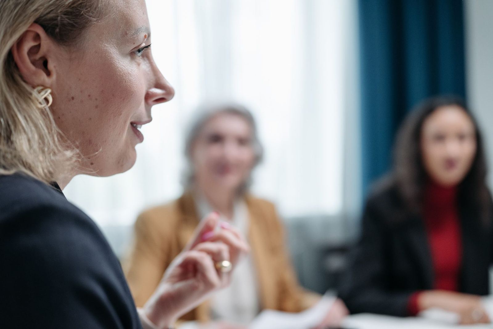 Mulher de perfil conduzindo uma conversa numa reunião, com as colegas atentas ao fundo