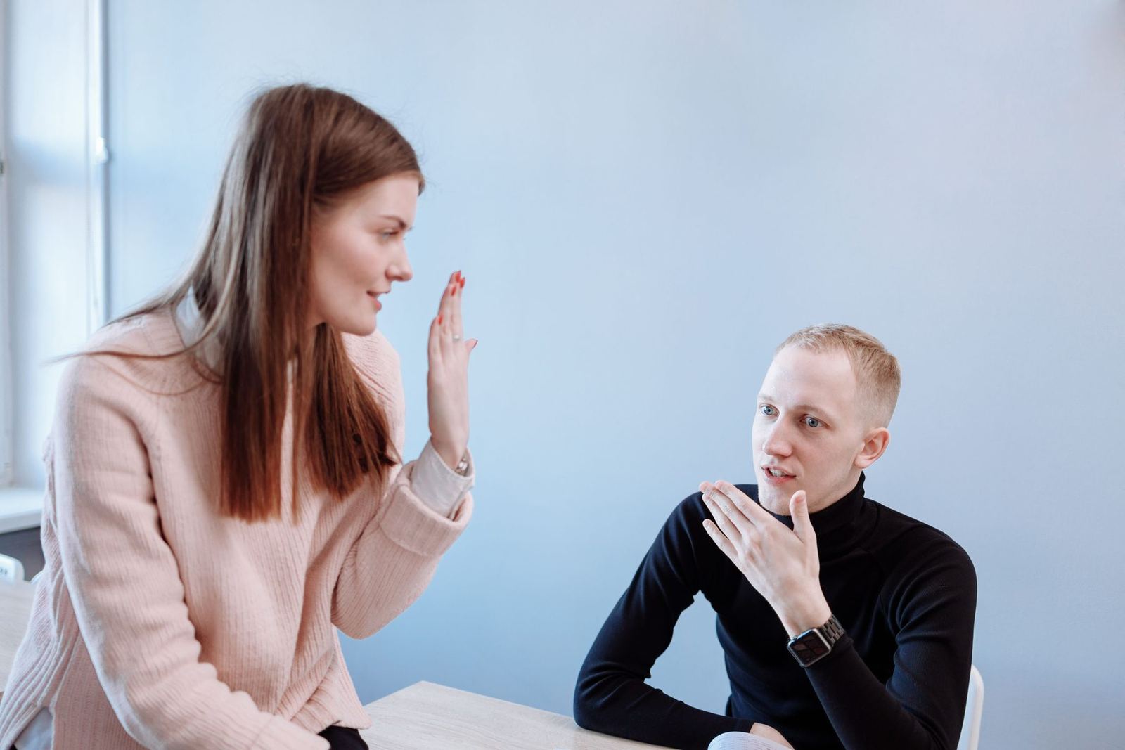 Mulher e homem conversando à mesa, os dois explicando com gestos das mãos