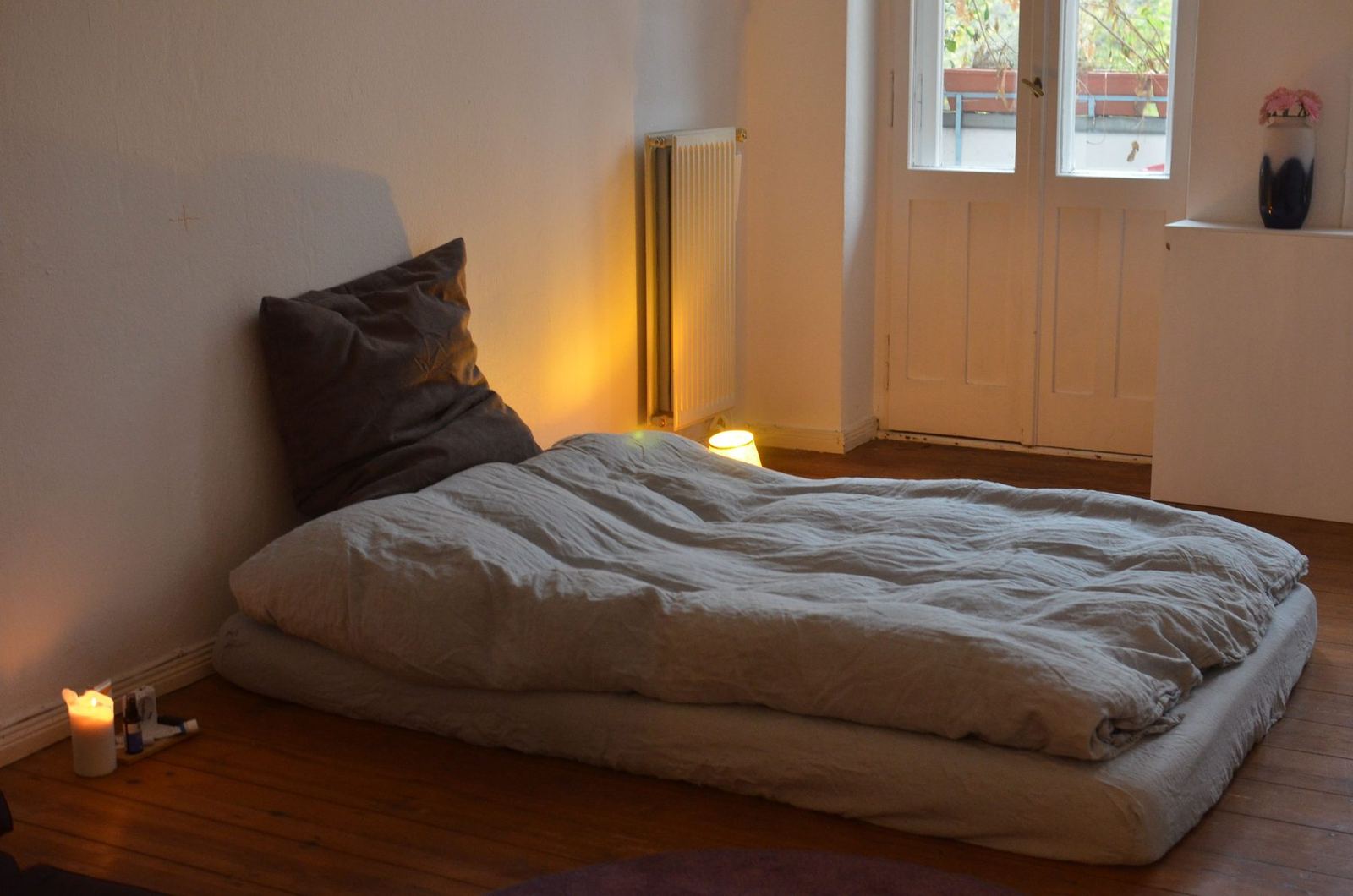 Quarto vazio à noite, com um colchão no chão, uma vela e uma luminária acesa
