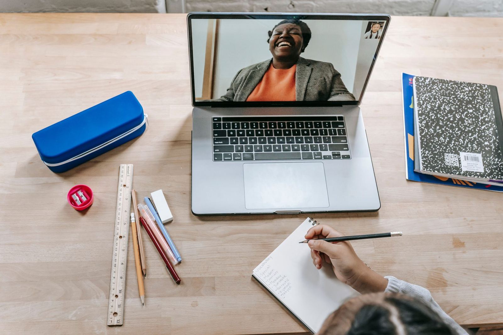 Aula ao vivo no notebook, com a professora rindo na tela e o caderno aberto ao lado