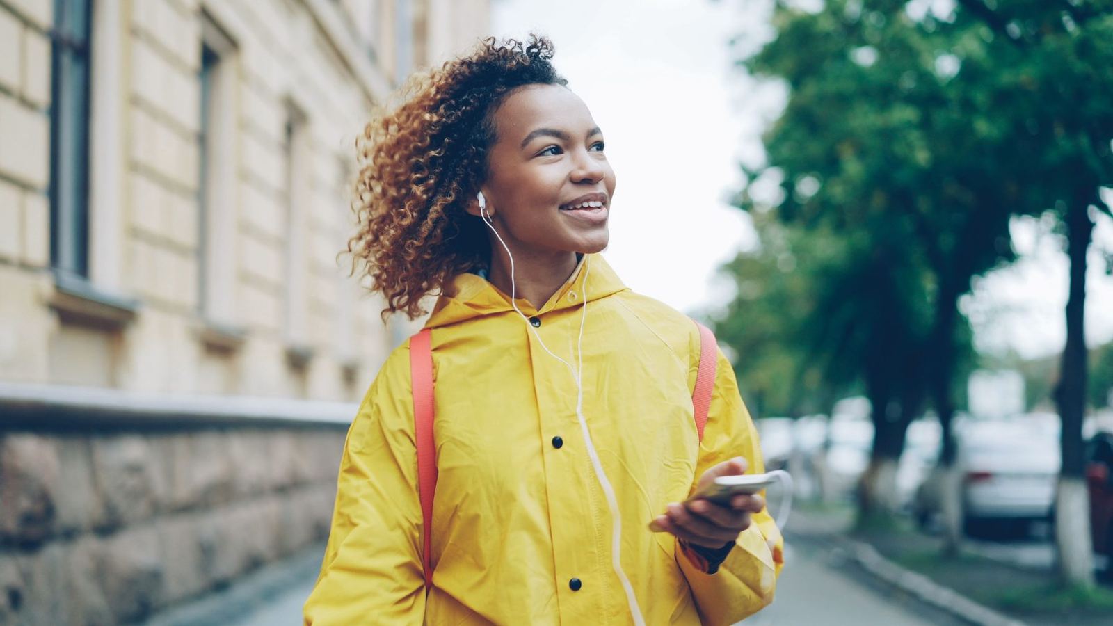 Mulher caminhando pela rua com fone de ouvido, sorrindo enquanto ouve