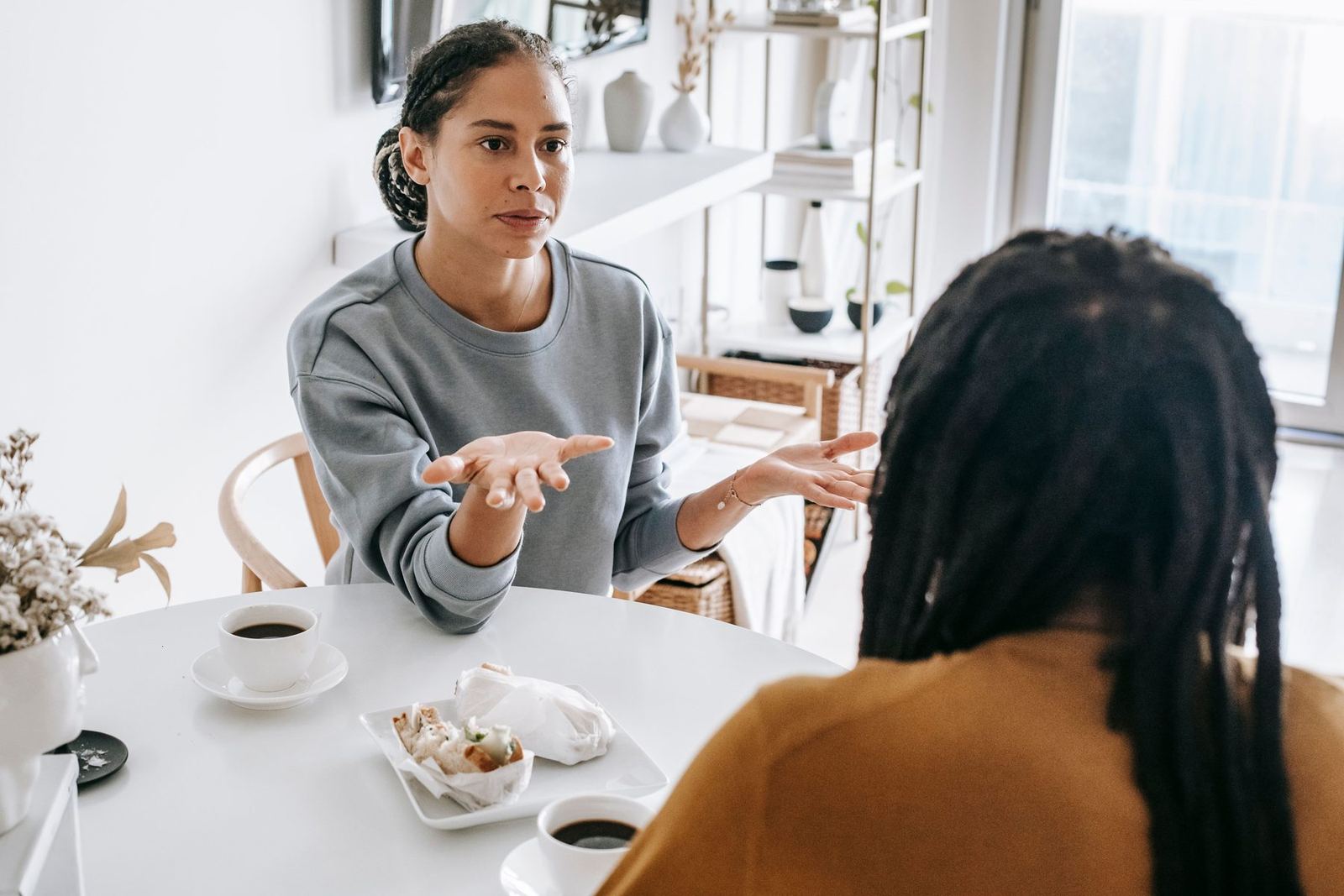 Mulher explicando algo com as mãos abertas, numa conversa à mesa do café